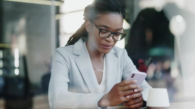 Positive woman black office manager browsing smartphone application social media texting messages smiling enjoying coffee break in cafeteria. Business people. Businesswoman.