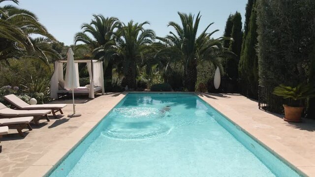Dolly forward shot of a fit young man diving into a swimming pool in a beautiful property