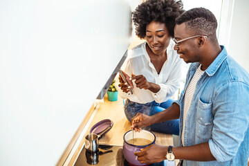 Beautiful young couple is using a smartphone and smiling while cooking in kitchen at home. Shot of a happy young couple using a digital tablet while preparing a healthy meal together at home