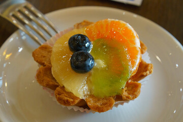 Photography of a delicious tartlet with orange, kiwi, blueberry, pineapple. Theme how to get good mood at the morning. Breakfast concept.