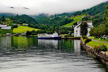 Obraz premium Cruise ferry docking in a small village in Geirangerfjord, with mist coming down the mountain
