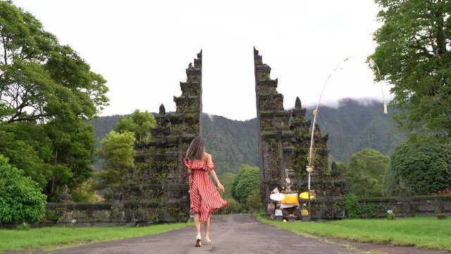Young happy traveler woman in red dress running toward iconic Handara Gate,Bali