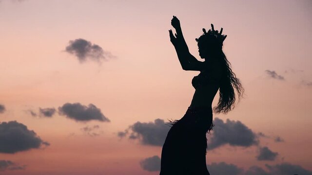 Close up of sexy, elegant and erotic arabian woman performing belly dance on the beach during golden hour. Silhouette. Side view. Slow motion.