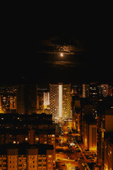 The moon is over the night city. Multi-storey houses with city lights. Night lights.