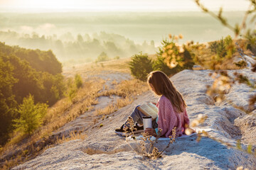 Girl is reading book, while is sitting against beautiful nature scenery. She is holding book in mountains. Summer vacations and Lifestyle concept