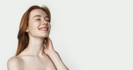 Obraz premium Ginger lady with freckles is wearing anti aging eye patches posing on white studio wall with naked shoulders advertising something