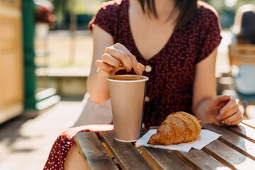 Close-up of a woman with cup of coffee and a croissant at a terrace in the morning light.