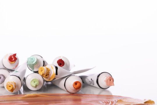 lot of open tubes of multicolored acrylic paint, lies on glass table close up. Wide strokes of paint in foreground. art exhibition invitation card isolated on white background