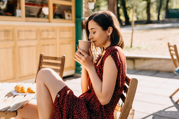 Young woman enjoying a cup of coffee, sitting at a cafe terrace in the morning. - Powered by Adobe