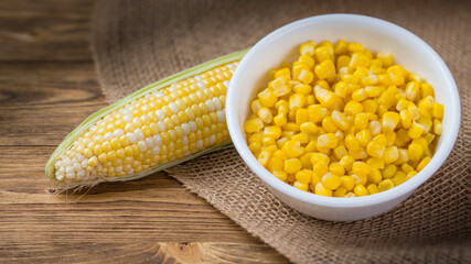 Bowl with corn seeds and ripe corn cobs on wooden table and burlap. Raw and tinned corn.