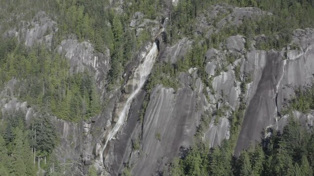 Quiet breathtaking stunning aerial hold close up of the mountain side of icy rushing waterfalls coming down ythe cliff covered trees of Shannon Falls BC Squamish in the summer. 1-5