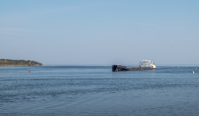 A merchant ship sails in the fairway among the buoys on a large lake or sea. Marine fleet, commercial transportation of goods. Horizontal orientation, selective focus.