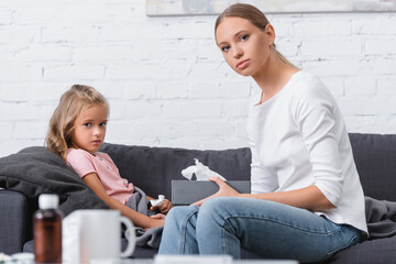Selective focus of woman holding box with napkins beside ill daughter on couch