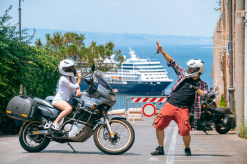 A couple of motorcycle riders happy dance. Love and relationships. Tourism and travel. Motorcycle for tours around the world. Street of sunny Italy. Ocean liner at sea in the background. Sorrento