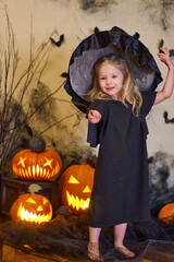 Halloween cute little girl dressed as a witch and a witch with a magic wand. Pumpkins and cobwebs. High quality photo
