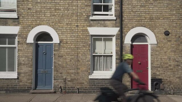 Front view of two typical houses entrance in cambridge city england uk while cyclist passing by fast. Brick buildings with blue and red wooden doors