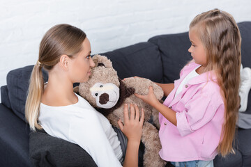 Daughter giving soft toy to ill mother on couch