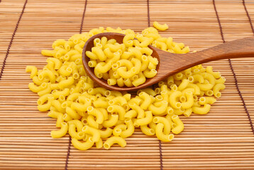 Closeup of dry elbow macaroni pasta and spoon on bamboo mat