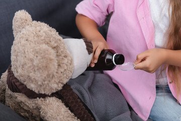 Cropped view of kid pouring syrup in spoon near teddy bear at home