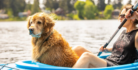 A woman and a golden retriever dog on a blue kayak over a lake