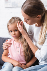 Selective focus of young woman touching forehead of ill daughter at home