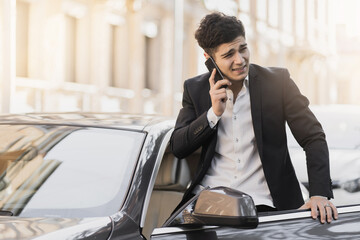 Strict black suit, white shirt. stylish male businessman manager, gets into the car talking on the phone with a partner. Strict black suit, white shirt