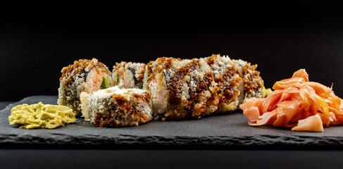 Panoramic photo of served warm sushi with ginger and wasabi on a black stone plate.