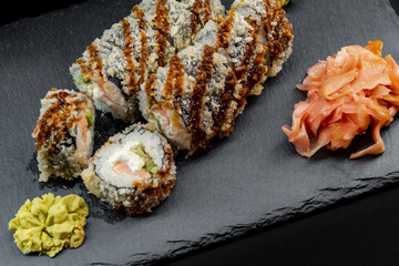 Served warm sushi with ginger and wasabi on a black stone plate.