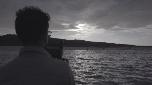 A man is using his camera to film a sunset near an island of the Galapagos islands in Ecuador.