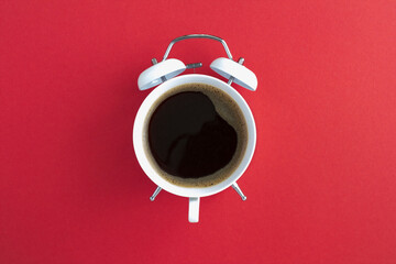 Top view of coffee on the dial of the white alarm clock in the center of the red background