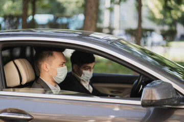 They are sitting in the car wearing protective masks from Covid 19, talking about work, strict business suits. businessmen managers and coronavirus, pandemic, epidemic, infection.