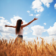 Happy woman enjoying the life in the field. Nature beauty, blue sky,white clouds and field with golden wheat. Outdoor lifestyle. Freedom concept. Woman jump in summer field