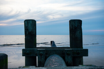 Fototapeta premium A Pipe With Wooden Poles on Each Side Sticking Out into the Ocean