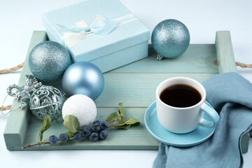 Beautiful Christmas composition with a gift box, a Cup of coffee balls and a branch with berries on a soft blue tray. Side view. The concept of the new year 2021 and Christmas.