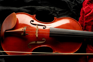 Close up of a violin with bow on a background of black and red fabrics