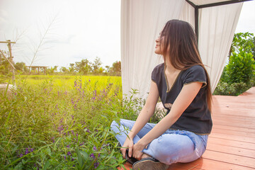 Young woman are smiling sitting on wooden bridge and rice field in farm and flowers. Relax on vacation concept. Holiday with natural.