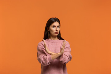Obraz premium It is forbidden. Portrait of serious woman in pink sweater, makes denial hand gesture, keeps arms crossed over chest, demonstrates stop sign, says no to something or somebody. on orange background
