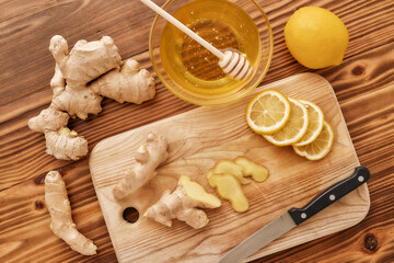 Preparation of cold and flu remedy cure drink, Top view of board, knife, fresh ginger, lemon, honey in a bowl with dipper on the wooden table