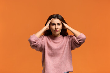 Whats happening. Stressful displeased beautiful woman, keeps hands on head, forgets something important, has displeased sad expression, does not know what to do, on orange background