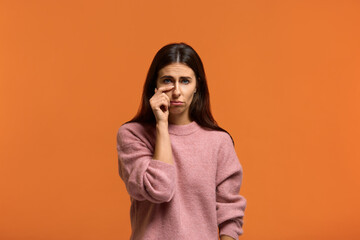 I want affection and attention. Portrait of beautiful woman in pink sweater cries, wipes tears, feels dejected, wants support. on orange background