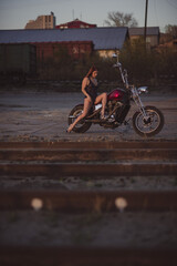 Red-haired woman in sexy lingerie in high heels sits on a motorcycle. Attractive red-haired girl sits on a motorcycle at sunset