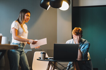 Tired young man working on a computer bowed his head, not paying attention to a colleague with...