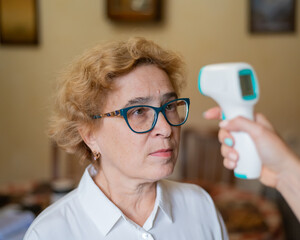 The doctor measures the temperature of an elderly woman with a non-contact infrared thermometer
