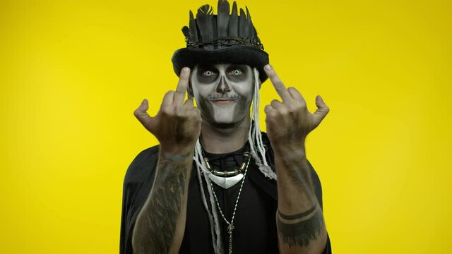 Sinister man with skull makeup making faces and showing middle finger. Bad manner gesture. Halloween