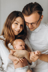 Portrait of parents with newborn baby, loving mom gently hold little daughter in arms, caring dad hold tiny hand of baby girl, smiling, enjoy happy moments, young family concept
