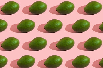 Trending style pattern of a whole green avocado on a pink background with hard light. Creative food texture.