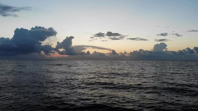 Calm ocean waters at dawn with clouds on the horizon