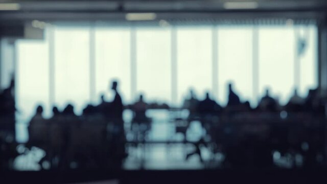 A defocused shot of many silhouettes of people walking around in a food court office building.