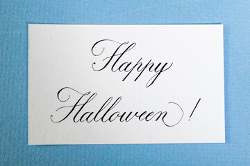 Calligraphic inscription Happy halloween on white textured paper, on blue paper card