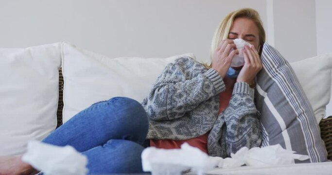 Sick woman with tissue sneezing while lying on couch at home
